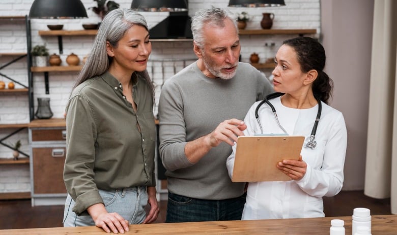 A doctor discusses medical information with an attentive older couple in a kitchen setting, creating a warm, collaborative atmosphere.